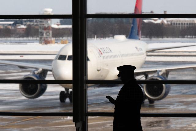 A pilot walks past a Delta Air Lines airplane as flights are delayed and cancelled following a significant winter storm at Ronald Reagan Washington National Airport in Arlington, Virginia, January 26, 2026. Millions of Americans were facing dangerously cold temperatures in the wake of a massive winter storm that whipped snow and ice across the country, knocking out power and paralyzing transportation. A frigid, potentially life-threatening Arctic air mass threatened to delay clean-up as municipalities from New Mexico to Maine tried to dig out following the storm, which dropped a vicious cocktail of heavy snow and wind along with freezing rain and sleet. (Photo by SAUL LOEB / AFP)