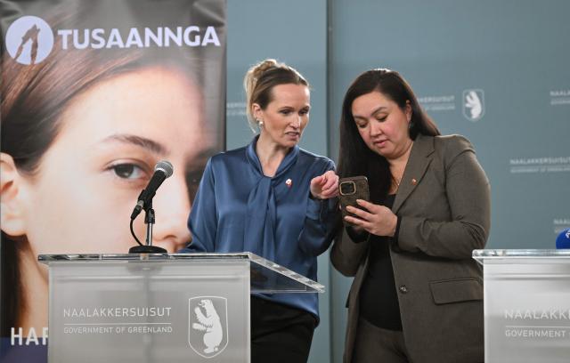 Nivi Olsen, Minister for Education, Culture, Sports and Church, Ministry for Education, Culture, Sports and Church, and Anna Wangenheim (L), Minister for Health and for Persons with Disabilities, look to a mobile phone before a press conference near then town hall in the city of Nuuk, western Greenland, on January 26, 2026. (Photo by Ina FASSBENDER / AFP)