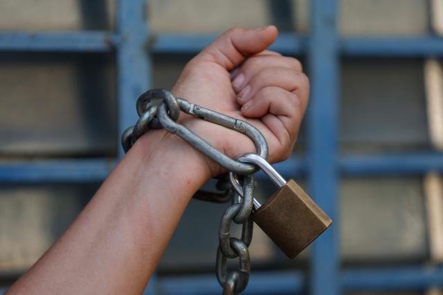 This view shows a person chained to a fence as they wait for news about the release of prisoners outside Zone 7 of the Bolivarian National Police (PNB) in the Sucre municipality of the Metropolitan District of Caracas (DMC) on January 26, 2026. More than 100 political prisoners were freed on the eve in Venezuela, where detainees are slowly being released under pressure from the United States, the non-governmental organization Foro Penal said. (Photo by Pedro MATTEY / AFP)