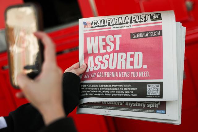 A person snaps a photo of the promotional print copy of the California Post newspaper during its launch day at the Larchmont Village neighborhood of Los Angeles, California on January 26, 2026. The California Post, a sister tabloid to the New York Post owned by Rupert Murdoch’s News Corp., launched on January 26 as a daily print and digital newspaper with coverage of news, sports, and entertainment. (Photo by Patrick T. Fallon / AFP)