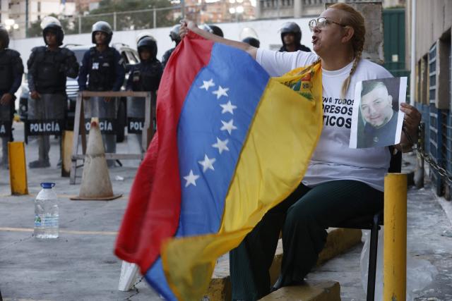 Evelis Cano, the mother of imprisoned Jack Tantak Cano, shouts slogans while holding a Venezuelan flag and chained to a railing as she waits for news about the release of prisoners outside Zone 7 of the Bolivarian National Police (PNB) in the Sucre municipality of the Metropolitan District of Caracas (DMC) on January 26, 2026. Evelis questions the slow process of political-prisoner releases announced on January 8 by Venezuelas interim government, under pressure from Washington after Nicolas Maduro was captured on January 3 in a US forces operation. (Photo by Pedro MATTEY / AFP)