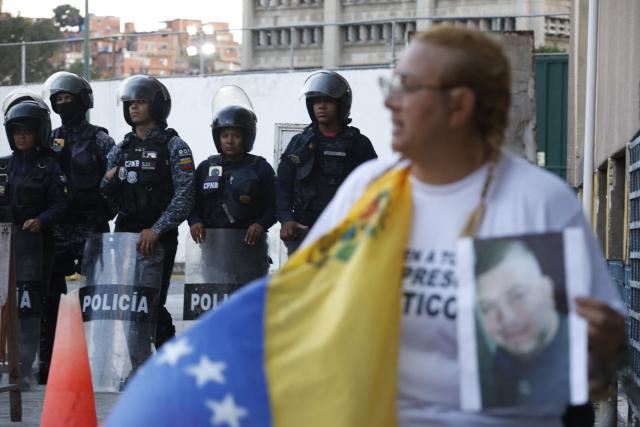 Evelis Cano, the mother of imprisoned Jack Tantak Cano, shouts slogans while holding a Venezuelan flag and chained to a railing as she waits for news about the release of prisoners outside Zone 7 of the Bolivarian National Police (PNB) in the Sucre municipality of the Metropolitan District of Caracas (DMC) on January 26, 2026. Evelis questions the slow process of political-prisoner releases announced on January 8 by Venezuelas interim government, under pressure from Washington after Nicolas Maduro was captured on January 3 in a US forces operation. (Photo by Pedro MATTEY / AFP)