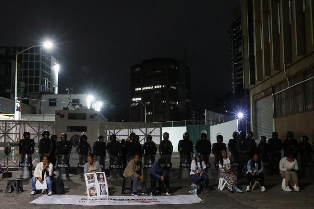 Women wait for news about the release of prisoners in front of members of the national police standing guard outside Zone 7 of the Bolivarian National Police (PNB) in the Sucre municipality of the Metropolitan District of Caracas (DMC) on January 26, 2026. More than 100 political prisoners were freed on the eve in Venezuela, where detainees are slowly being released under pressure from the United States, the non-governmental organization Foro Penal said. (Photo by Pedro MATTEY / AFP)