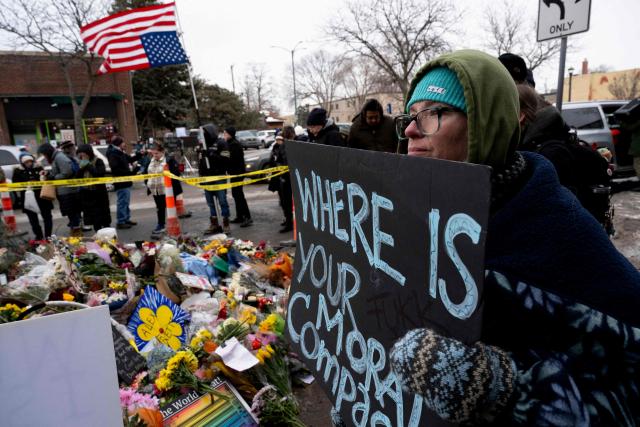 A woman holds a sign while visiting the makeshift memorial in the area where Alex Pretti was shot and killed by Federal immigration agents in Minneapolis, Minnesota, on January 26, 2026. On January 24, federal agents shot and killed Alex Pretti, a 37-year-old ICU nurse, while scuffling with him on an icy roadway in Minneapolis, less than three weeks after an immigration officer fired on Renee Good, also 37, killing her in her car. US President Donald Trump blamed their deaths on Democratic "chaos," as his administration faced intensifying pressure over its mass immigration crackdown in Minneapolis. (Photo by ROBERTO SCHMIDT / AFP)