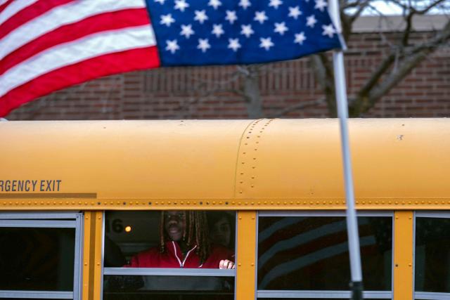 A student riding in a school bus looks at the crowd visiting the makeshift memorial in the area where Alex Pretti was shot and killed by federal immigration agents in Minneapolis, Minnesota, on January 26, 2026. On January 24, federal agents shot and killed Alex Pretti, a 37-year-old ICU nurse, while scuffling with him on an icy roadway in Minneapolis, less than three weeks after an immigration officer fired on Renee Good, also 37, killing her in her car. US President Donald Trump blamed their deaths on Democratic "chaos," as his administration faced intensifying pressure over its mass immigration crackdown in Minneapolis. (Photo by ROBERTO SCHMIDT / AFP)
