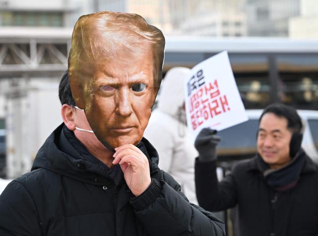 A protester wears a mask of US President Donald Trump during a rally condemning Trump's plans to raise tariffs on South Korea in front of the US embassy in Seoul on January 27, 2026. US President Donald Trump said January 26, that he would raise tariffs on South Korean goods including autos, lumber and pharmaceuticals, accusing the country of not living up to an earlier trade pact struck with Washington. (Photo by Jung Yeon-je / AFP)