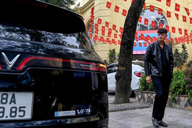 A man walks past a Vinfast electric car on a street in Hanoi on January 27, 2026. Vietnam's first homegrown electric car manufacturer is partnering with Israeli AI firm Autobrains to upgrade its autonomous driving technology and launch a lower-cost "robo-car" system, VinFast said on January 27, 2026. (Photo by Nhac NGUYEN / AFP)