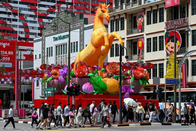 TOPSHOT - Pedestrians cross a street next to a Lunar New Year of the Horse decoration in the Chinatown district of Singapore on January 27, 2026. (Photo by Roslan RAHMAN / AFP)