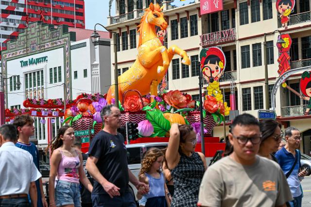 Pedestrians cross a street next to a Lunar New Year of the Horse decoration in the Chinatown district of Singapore on January 27, 2026. (Photo by Roslan RAHMAN / AFP)