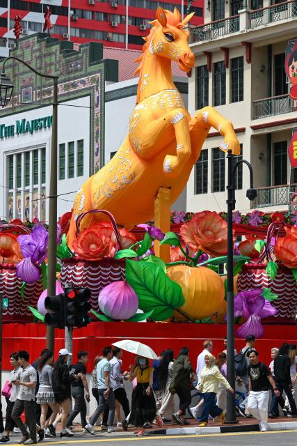 Pedestrians cross a street next to a Lunar New Year of the Horse decoration in the Chinatown district of Singapore on January 27, 2026. (Photo by Roslan RAHMAN / AFP)