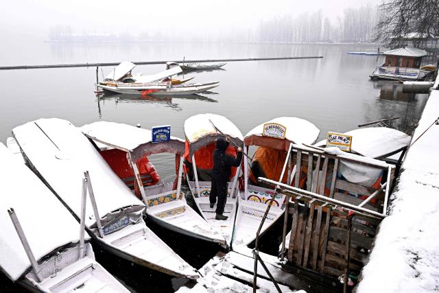 A man clears snow after a spell of fresh snowfall at the Dal lake in Srinagar on January 27, 2026. (Photo by Tauseef MUSTAFA / AFP)