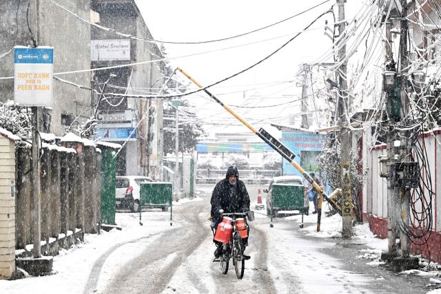 A man carries milk canisters on his bicycle during a spell of fresh snowfall in Srinagar on January 27, 2026. (Photo by Tauseef MUSTAFA / AFP)