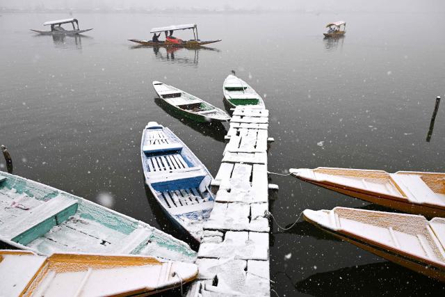 TOPSHOT - A boatman steers a shikara during a spell of fresh snowfall at the Dal lake in Srinagar on January 27, 2026. (Photo by Tauseef MUSTAFA / AFP)
