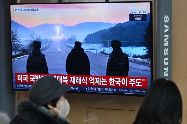 TOPSHOT - People sit in front of a television screen showing a news broadcast with file footage of a North Korean missile test, at a train station in Seoul on January 27, 2026. North Korea fired at least two ballistic missiles towards the Sea of Japan, a day after a top Pentagon official visited the peninsula and hailed Washington's "model ally" in the South. (Photo by Jung Yeon-je / AFP)