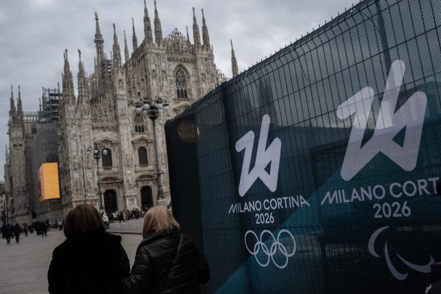 People walk past fences displaying the logo of Milano Cortina 2026 Olympic Games in Duomo’s square, in Milan on January 27, 2026. (Photo by MARCO BERTORELLO / AFP)