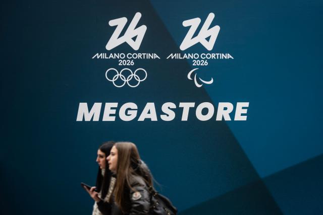 People walk past a banner of the Megastore for Milano Cortina 2026 Olympic Games at Piazza Duomo in Milan on January 27, 2026. (Photo by MARCO BERTORELLO / AFP)