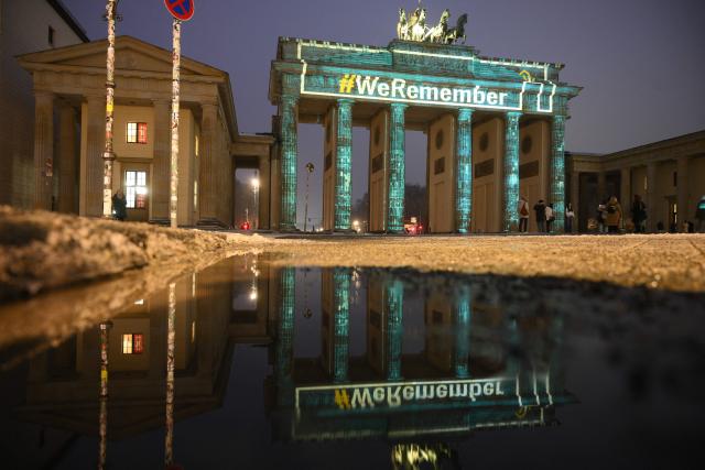 The slogan "We Remember" is projected with lights on the Branbenburg Gate as its reflection is seen on a water puddle in Berlin, Germany, on January 27, 2026, during commemorations of the International Holocaust Remembrance Day. (Photo by RALF HIRSCHBERGER / AFP)