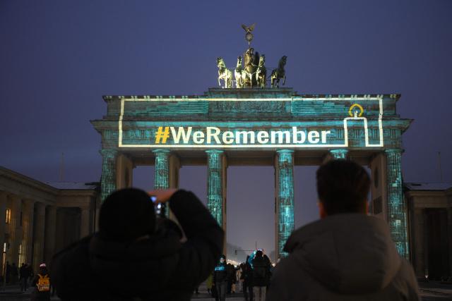 The slogan "We Remember" is projected with lights on the Branbenburg Gate as people stand in front of it in Berlin, Germany, on January 27, 2026, during commemorations of the International Holocaust Remembrance Day. (Photo by RALF HIRSCHBERGER / AFP)