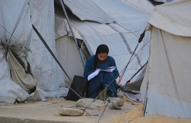 A Palestinian woman writes on a book while seated near tents in Khan Yunis in the southern Gaza Strip on January 27, 2026. Since October 10, a fragile US-sponsored truce in Gaza has largely halted the fighting between Israeli forces and Hamas, but both sides have alleged frequent violations. (Photo by Bashar Taleb / AFP)