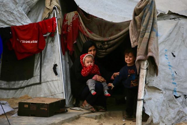 A Palestinian woman sits with children inside a tent in Khan Yunis in the southern Gaza Strip on January 27, 2026. Since October 10, a fragile US-sponsored truce in Gaza has largely halted the fighting between Israeli forces and Hamas, but both sides have alleged frequent violations. (Photo by Bashar Taleb / AFP)
