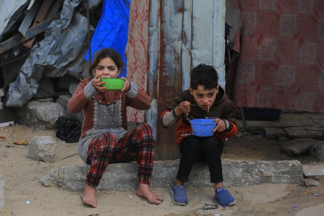Palestinians children eat their food portions received in Khan Yunis in the southern Gaza Strip on January 27, 2026. Since October 10, a fragile US-sponsored truce in Gaza has largely halted the fighting between Israeli forces and Hamas, but both sides have alleged frequent violations. (Photo by Bashar Taleb / AFP)