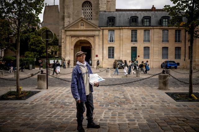 (FILES) Pakistani born 73-year-old newspaper hawker Ali Akbar poses as he sells newspaper copies in the street of the Latin Quarter in Paris on September 16, 2025. Akbar, the last remaining newspaper vendor of the French capital, will be awarded by France's President as knight in the National Order of Merit. (Photo by Guillaume BAPTISTE / AFP)