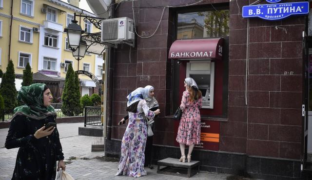 (FILES) Chechen women wait in front of an ATM machine (automatic teller machine) in downtown Grozny at the Avenue of Vladimir Putin on July 26, 2019. The main city street, Prospekt Pobedy (Victory Avenue), was named after Russian President Vladimir Putin in 2008. (Photo by Alexander NEMENOV / AFP)