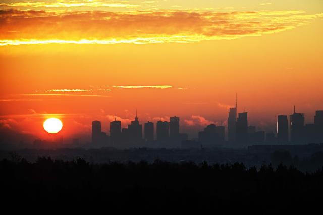 (FILES) The sun rises above Warsaw's skyscrapers as seen from the village of Klaudyn, Masovian Voivodeship on November 7, 2025. Unemployment was soaring and the country was in economic turmoil when Monika Pudlik first left Poland to find a job in Ireland just over two decades ago. Now, Poland is thriving and, like tens of thousands of her fellow citizens, she is planning to return to her home in the central city of Plock. (Photo by Sergei GAPON / AFP)