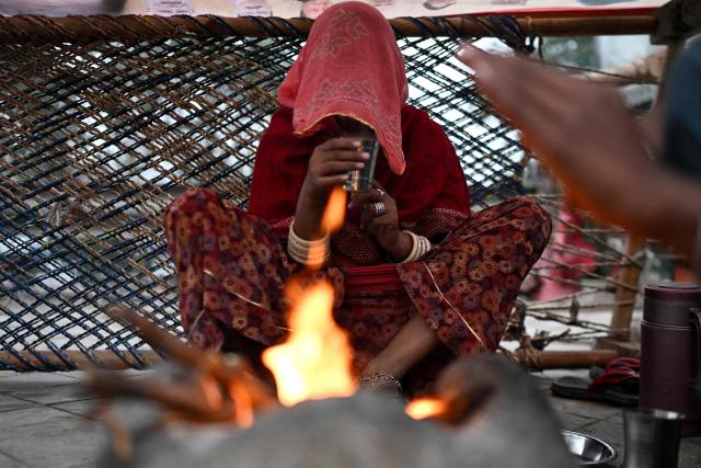 A veiled woman drinks tea beside a bonfire during a cold winter morning in New Delhi on January 28, 2026. (Photo by Arun SANKAR / AFP)
