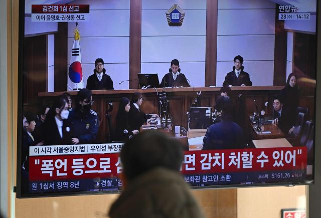 A man watches a television screen showing a live broadcast of the trial verdict on corruption charges of South Korea's former first lady Kim Keon Hee (L with a mask on the screen), at a train station in Seoul on January 28, 2026. A South Korean judge handed the country's former first lady Kim Keon Hee 20 months in jail for corruption on January 28, but acquitted her for alleged stock manipulation and other charges. (Photo by Jung Yeon-je / AFP)
