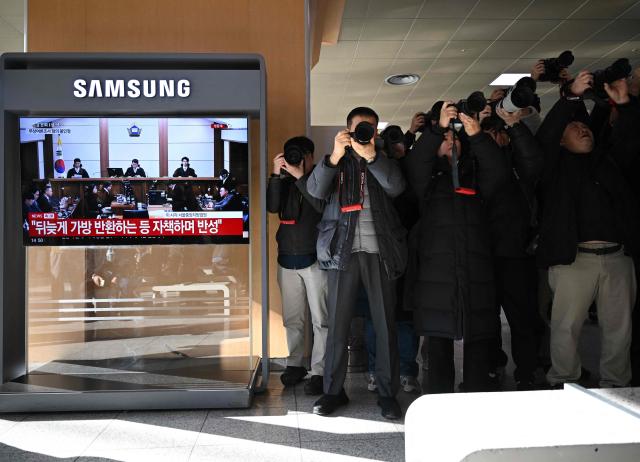 TOPSHOT - Photographers take pictures next to a television screen showing a live broadcast of the trial verdict on corruption charges of South Korea's former first lady Kim Keon Hee (R with a mask on the screen), at a train station in Seoul on January 28, 2026. A South Korean judge handed the country's former first lady Kim Keon Hee 20 months in jail for corruption on January 28, but acquitted her for alleged stock manipulation and other charges. (Photo by Jung Yeon-je / AFP)