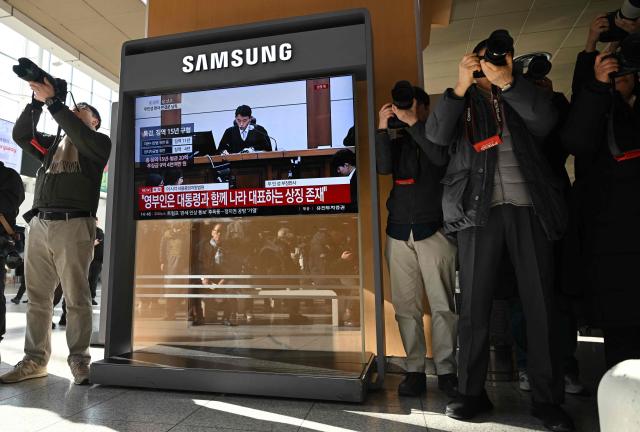 Photographers take pictures next to a television screen showing a live broadcast of the trial verdict on corruption charges of South Korea's former first lady Kim Keon Hee, at a train station in Seoul on January 28, 2026. A South Korean judge handed the country's former first lady Kim Keon Hee 20 months in jail for corruption on January 28, but acquitted her for alleged stock manipulation and other charges. (Photo by Jung Yeon-je / AFP)