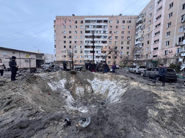 People stand by a crater left in an area hit by an air attack in Zaporizhzhia on January 28, 2026, amid the Russian invasion of Ukraine. (Photo by Darya NAZAROVA / AFP)