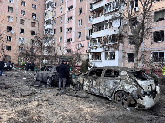 People stand next to burned cars and a damaged residential building in an area hit by an air attack in a residential neighborhood in Zaporizhzhia on January 28, 2026, amid the Russian invasion of Ukraine. (Photo by Darya NAZAROVA / AFP)