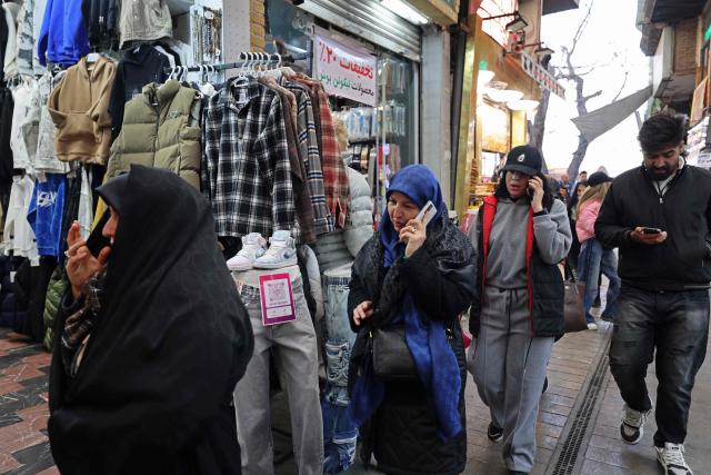 People use their mobile phones while walking through the Tajrish Bazaar in Tehran on January 28, 2026. (Photo by ATTA KENARE / AFP)