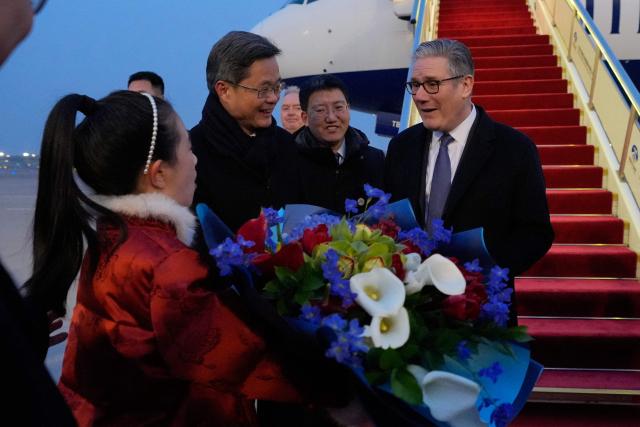 Britain's Prime Minister Keir Starmer receives a bouquet of flowers upon his arrival at an airport in Beijing on January 28, 2026. (Photo by Kin Cheung / POOL / AFP)