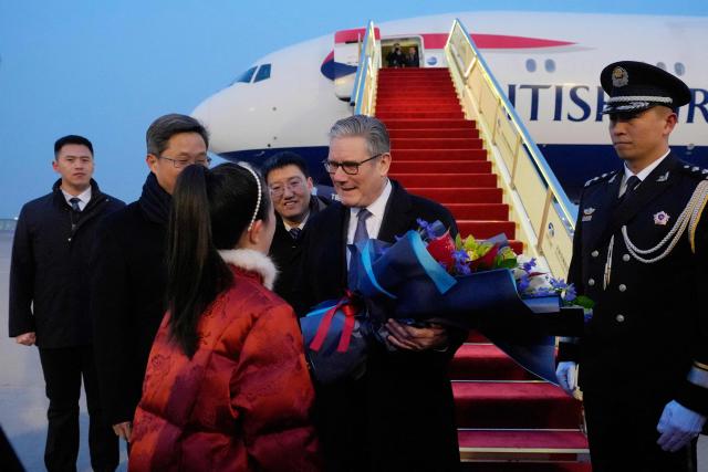 Britain's Prime Minister Keir Starmer receives a bouquet of flowers upon his arrival at an airport in Beijing on January 28, 2026. (Photo by Kin Cheung / POOL / AFP)