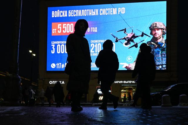 People pass by a digital screen displaying an ad promoting contract military service in the Russian army's unmanned systems units in Saint Petersburg on January 28, 2026. (Photo by Olga MALTSEVA / AFP)