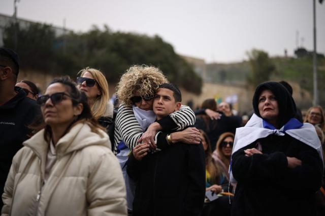 TOPSHOT - Mourners with the Israeli flag around their shoulders attend the funeral of Israeli hostage Ran Gvili, whose remains were finally brought back to Israel on January 26, in the southern town of Meitar on January 28, 2026. Grieving relatives of Ran Gvili gathered on January 28, 2026, as Israel prepared to bury the last hostage returned from Gaza, marking the end of a painful national saga triggered by Hamas's 2023 attack. Israeli forces on January 26 brought home the remains of Gvili, a police officer who was killed in action during Hamas's attack on October 7, 2023 which triggered the devastating war in Gaza. (Photo by ilia yefimovich / AFP)