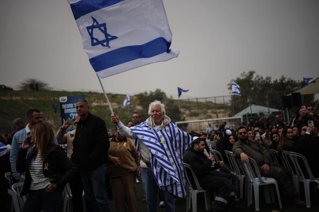 A man waves the Israeli flag as mourners gather for the funeral of Israeli hostage Ran Gvili, whose remains were finally brought back to Israel on January 26, in the southern town of Meitar on January 28, 2026. Grieving relatives of Ran Gvili gathered on January 28, 2026, as Israel prepared to bury the last hostage returned from Gaza, marking the end of a painful national saga triggered by Hamas's 2023 attack. Israeli forces on January 26 brought home the remains of Gvili, a police officer who was killed in action during Hamas's attack on October 7, 2023 which triggered the devastating war in Gaza. (Photo by ilia yefimovich / AFP)