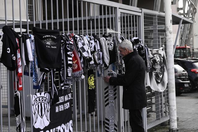 A man places a scarf of Paok while mourning at a makeshift memorial outside of the Toumba stadium also known as the PAOK stadium in Thessaloniki on January 28, 2026, following the fatal collision of a minibus transporting Greek football fans with a truck in Romania. A minibus transporting Greek football fans collided with a truck in Romania on January 27, 2026, leaving seven dead and three injured, officials said. The minibus carrying 10 men was travelling from Greece to France where the fans were planning to attend the Europa League match between PAOK and Lyon on January 29, 2026, when it collided with a truck in Timis county in western Romania, local police said. (Photo by SAKIS MITROLIDIS / AFP)