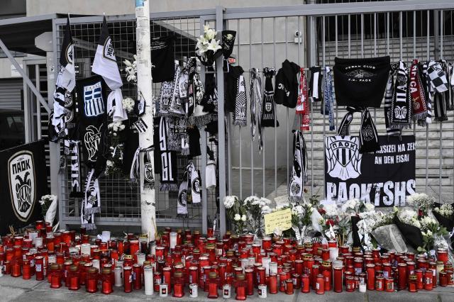 This photograph shows candles and flowers at a makeshift memorial outside of the Toumba stadium also known as the PAOK stadium in Thessaloniki on January 28, 2026, following the fatal collision of a minibus transporting Greek football fans with a truck in Romania. A minibus transporting Greek football fans collided with a truck in Romania on January 27, 2026, leaving seven dead and three injured, officials said. The minibus carrying 10 men was travelling from Greece to France where the fans were planning to attend the Europa League match between PAOK and Lyon on January 29, 2026, when it collided with a truck in Timis county in western Romania, local police said. (Photo by Sakis Mitrolidis / AFP)