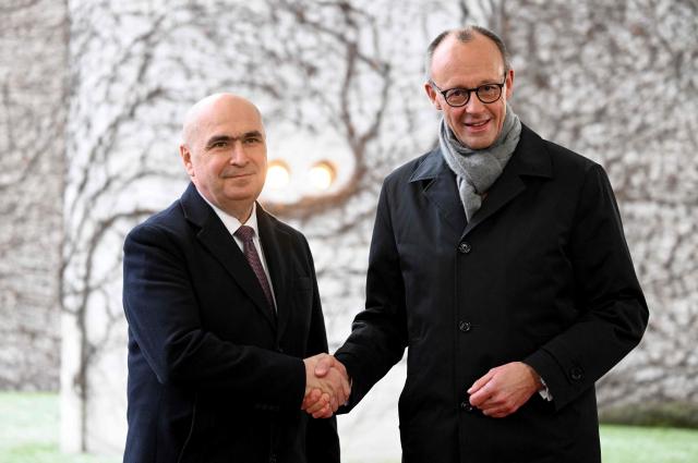 German Chancellor Friedrich Merz (R) shakes hands with Romania's Prime Minister Ilie Bolojan as he arrives for a visit at the Chancellery in Berlin, Germany. (Photo by RALF HIRSCHBERGER / AFP)