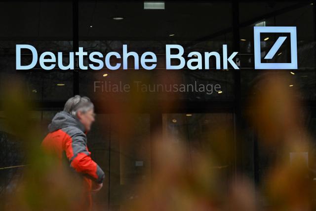 A passer-by walks past Deutsche Bank headquarters in Frankfurt am Main, on January 28, 2028, as German prosecutors and police on searched the bank's headquarters in an investigation over suspected money laundering offences, officials said. According to the Sueddeutsche Zeitung newspaper, the probe is connected to suspected offences in the bank's dealings with companies linked to Russian billionaire businessman Roman Abramovich. Prosecutors confirmed the raids but did not say who was being targeted. (Photo by Kirill KUDRYAVTSEV / AFP)