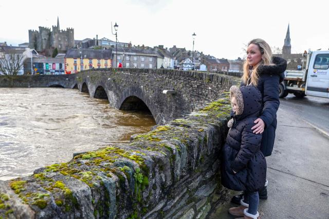 People stand on the corner of Barkers Bridge looking at the height of the River Slaney, after the river burst its banks during Strom Chandra, in Enniscorthy, near Wexford, south east Ireland on January 28, 2026. (Photo by Paul Faith / AFP)