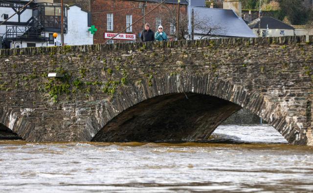 People walk on Barkers Bridge spanning the River Slaney, after the river burst its banks during Strom Chandra, in Enniscorthy, near Wexford, south east Ireland on January 28, 2026. (Photo by Paul Faith / AFP)