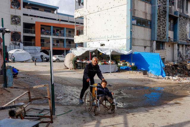 A man pushes a child sitting in a wheelchair outside a make-shift camp for those displaced by conflict in Al-Rimal school run by the United Nations Relief and Works Agency for Palestine Refugees (UNRWA) in the northern Gaza Strip on January 28, 2026. Since October 10, a fragile US-sponsored truce in Gaza has largely halted the fighting between Israeli forces and Hamas, but both sides have alleged frequent violations. (Photo by Omar AL-QATTAA / AFP)
