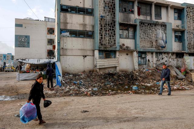 People walk outside a make-shift camp for those displaced by conflict in Al-Rimal school run by the United Nations Relief and Works Agency for Palestine Refugees (UNRWA) in the northern Gaza Strip on January 28, 2026. Since October 10, a fragile US-sponsored truce in Gaza has largely halted the fighting between Israeli forces and Hamas, but both sides have alleged frequent violations. (Photo by Omar AL-QATTAA / AFP)
