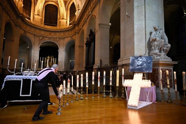 An attendee adjusts candles placed around a cross and a portait picture of late French actress Brigitte Bardot during a memorial mass at Saint-Roch church in Paris, on January 28, 2026. (Photo by JULIEN DE ROSA / AFP)