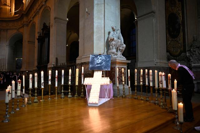 An attendee adjusts candles placed around a cross and a portait picture of late French actress Brigitte Bardot during a memorial mass at Saint-Roch church in Paris, on January 28, 2026. (Photo by JULIEN DE ROSA / AFP)